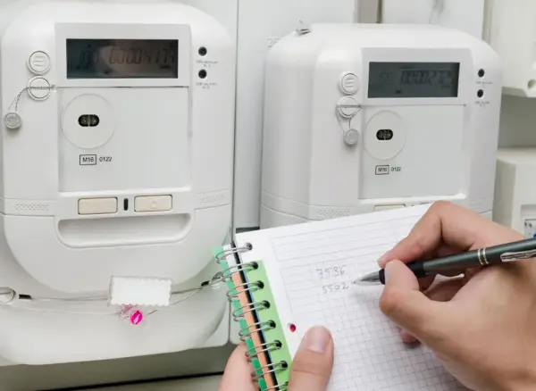 Osoba notuje odczyty liczników energii elektrycznej, przygotowując się do rozliczenia opłaty za przesył prądu.