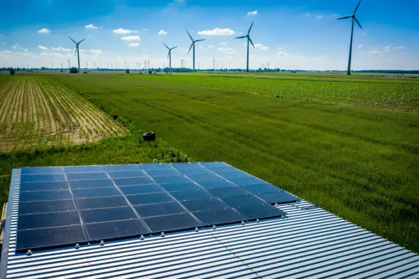 Panele słoneczne na dachu i wiatraki na polu, symbolizujące program agroenergia i zrównoważony rozwój.